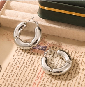 Detailed view of silver hollow bamboo-style C-shape earrings on vintage paper