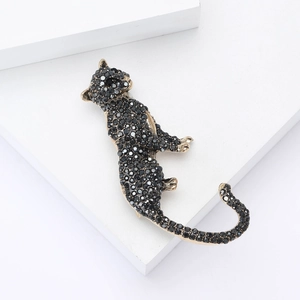 Close-up of golden leopard brooch with black rhinestones on a minimalist white stand