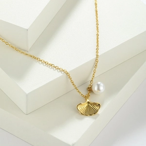 Detailed macro view of the golden ginkgo leaf pendant with a white pearl on a fine chain