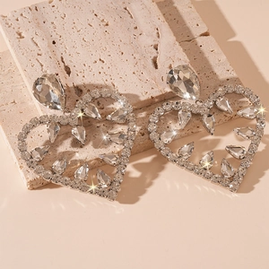 Macro shot of oversized heart drop earrings with sparkling rhinestones on beige stone