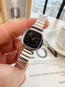 Close-up of a ladies' square black dial watch with a silver metal band on a magazine