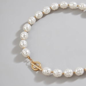 Baroque pearl necklace with gold T-bar clasp shown against a minimalist grey background