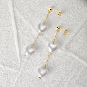 Detailed view of long gold chain earrings with white heart-shaped pearl drop charms