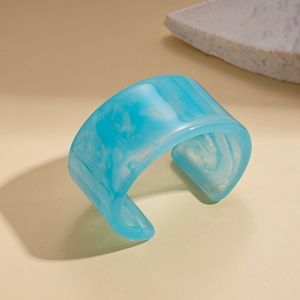 Detailed view of wide resin bangle featuring light blue marble texture on textured background