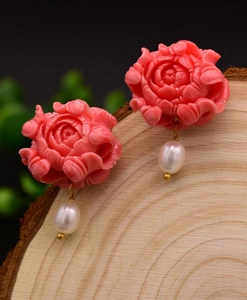 Macro detail of hand-carved pink floral earrings with white pearls on a wooden block