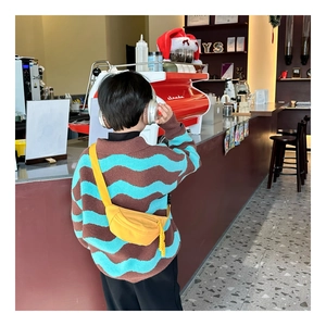 Kids yellow nylon chest bag worn over a striped knit sweater in a cafe setting