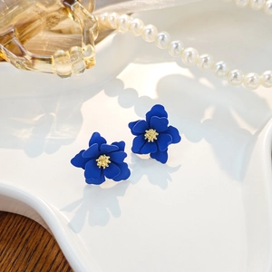 Macro shot of dark blue flower earrings with golden stamens on a ceramic plate