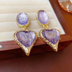 Vintage gold textured oval earrings with purple heart charms on a velvet jewelry tray