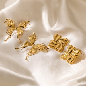 Golden butterfly and knot stainless steel stud earrings on white silk background