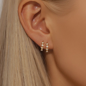 Close-up of elegant gold drop earrings with three clear zircons on a model's ear