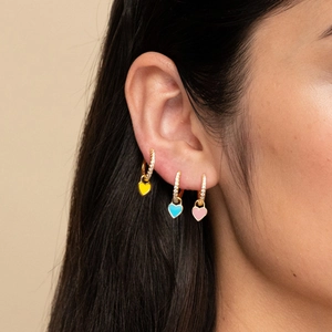 Three gold heart earrings with zircon inlay and colorful enamel pendants on ear