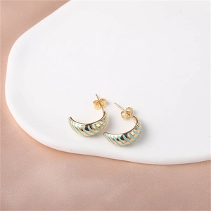 Detailed shot of golden enamel hoop earrings with blue stripes on a ceramic tray