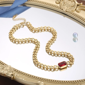 Detail van gouden Cubaanse ketting met een rechthoekige rode kristallen hanger op spiegel