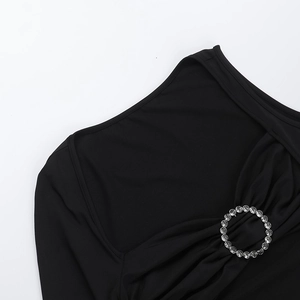 Detail of a black knit dress featuring a one-shoulder neckline with a rhinestone buckle