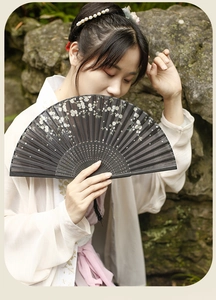 Close-up of a black folding fan with white plum blossom patterns held by a model in Hanfu
