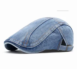 Detail of blue denim beret cap showing orange stitching and adjustable metal buckle