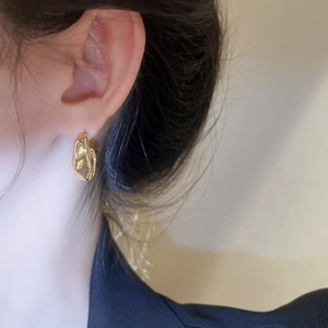 Close-up of a model wearing irregular gold lava texture geometric C-shaped stud earrings