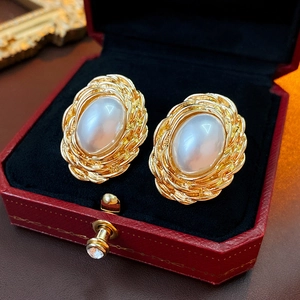 Close-up of vintage oval pearl earrings in gold woven frame within a red velvet box