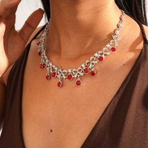 Detailed view of silver bow necklace with vibrant red teardrop crystals on model