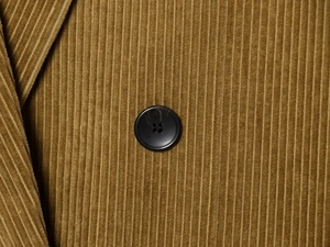 Detail of mustard yellow corduroy fabric with a black four-hole button on the blazer