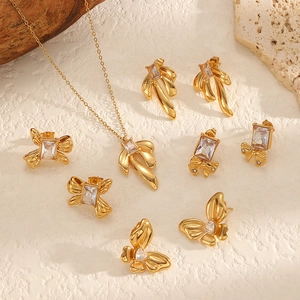 Set aus goldener Schleifenkette und Zirkonia-Ohrringen auf minimalistischem Steingrund