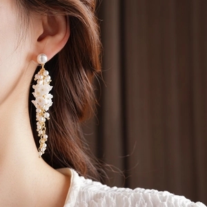 Detail of long gold tassel earrings with white resin flowers and delicate faux pearls