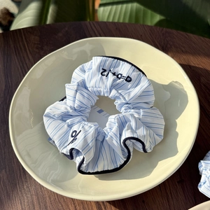 Detailed shot of blue and white striped scrunchie with embroidery on beige plate
