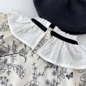 Close-up of floral baby top with ruffled collar and black velvet ribbon detail