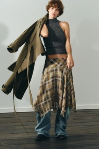 Détail d'une tenue superposée avec haut en tricot gris, jupe à carreaux et jean en studio