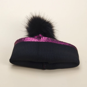 Dettaglio del berretto in maglia con paillettes rosa metallizzato e pompon di pelliccia
