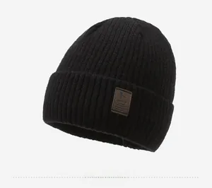 Close-up of black ribbed knit beanie with brown leather brand patch on white background