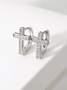 Close-up of silver cross pendant earrings with micro-set zircons on white geometric steps