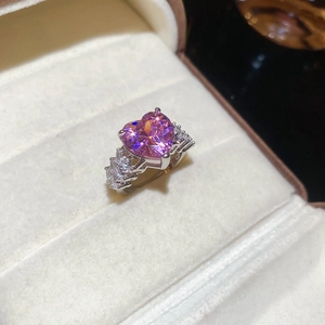 Close-up of pink heart-shaped zircon ring with side stones on beige velvet cushion