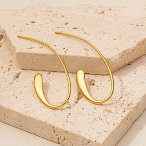 Detailed view of 18K gold-plated stainless steel curved earrings on a beige stone slab