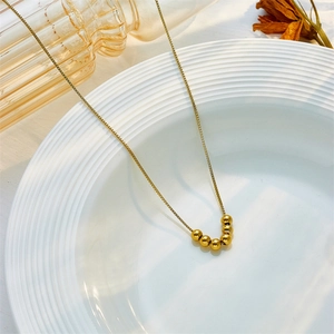 Minimalistische goldene Titanstahlkette mit Perlen auf weißem Teller bei natürlichem Licht