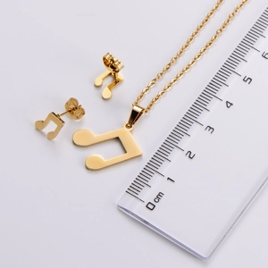 Detailed view of gold music note jewelry set with necklace and studs next to a scale ruler
