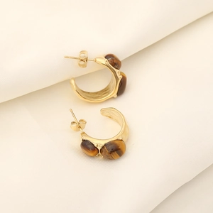 Close-up of golden hoop earrings with tiger eye stone inlays on beige fabric background