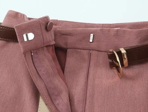 Detail der rosafarbenen Hose mit verdecktem Reißverschluss und braunem Gürtel
