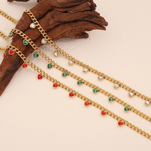 Gold chain necklaces with red green and clear heart pendants on a rustic wood background
