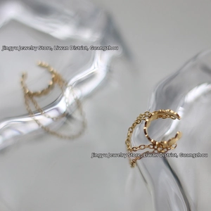 Detailed view of golden wave-textured ear cuff with fine chain tassels on glass