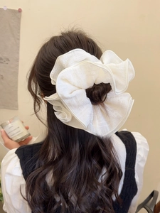 Close-up of a large white layered pleated scrunchie styled on a classic bun hairstyle