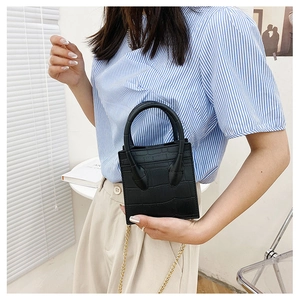 Detail of black faux crocodile leather texture and golden chain strap on a mini tote bag