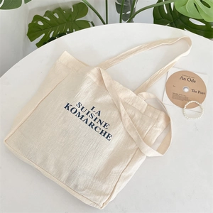 Detail of a minimalist cream canvas tote bag with navy blue text print on a clean table