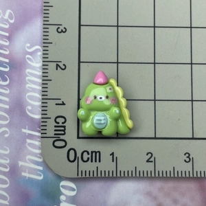 Size measurement of a mini green resin dinosaur charm on a scale showing 1.8cm height