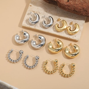 Chunky gold and silver C-shaped hoop earrings displayed on textured stone and wood