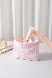 Détail d'une trousse à maquillage à carreaux roses avec motif nœud brodé et zip métallique