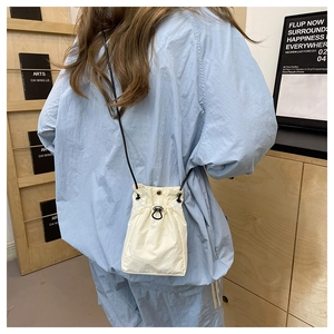 Detailed view of beige nylon drawstring mini bucket bag with black thin shoulder straps