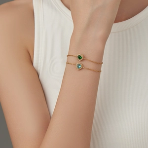 Elegant gold heart bracelets set with green and blue crystals on a female wrist