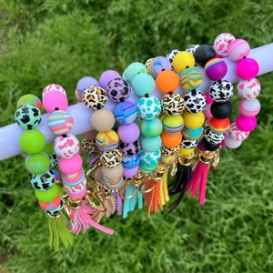 Colorful silicone beaded wristlet keychains with leather tassels on a green lawn