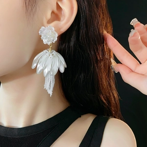 Detail view of white flower earrings with pearl tassels worn by a model in soft lighting